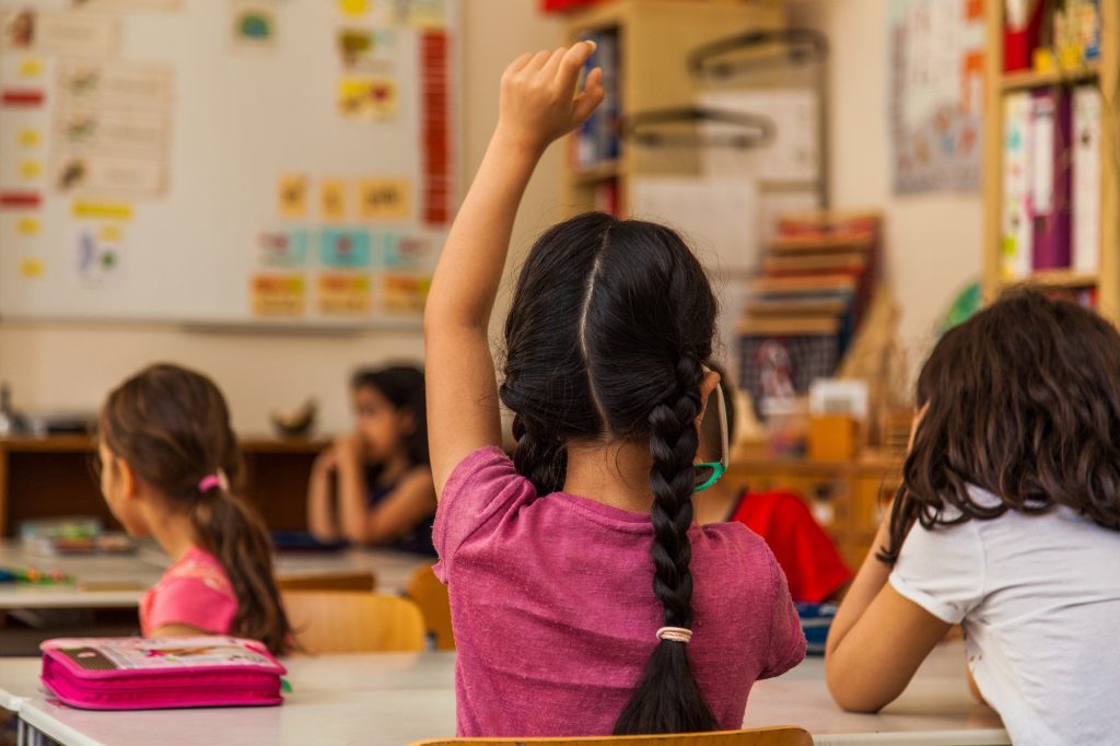Kinder im Unterricht, ein Kind meldet sich mit erhobener Hand